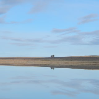 A still lake reflecting the sky and the low, open Patagonian steppe