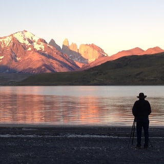 A visitor beside Laguna Amarga with sunlit mountains reflected in the water