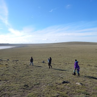 Visitors walking across open grassland beside a shallow lake