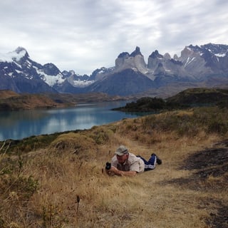 A visitor resting on a grassy hillside above a lake in Torres del Paine