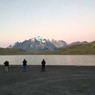 Three visitors beside a lake with the mountains of Torres del Paine in the early light